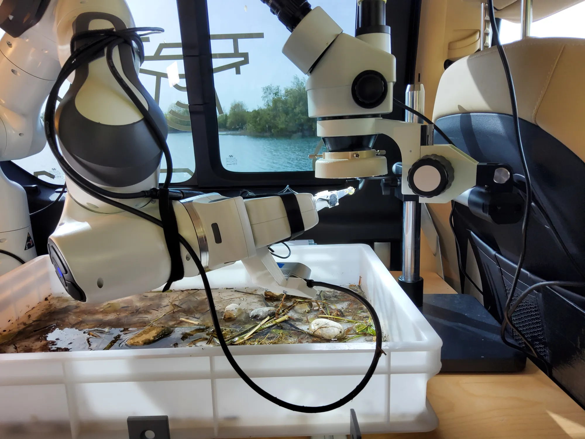 Environmental Robotics in the Field. Shown is a robotic arm, mounted in a vehicle serving as a mobile robot hub. The robot is equipped with an elastic finger pair, grasping a small piece of algae and positioning it beneath a microscope for analysis.